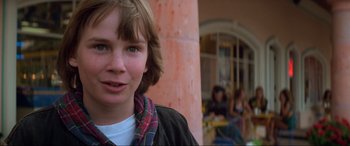 Movie still from “Last Action Hero” (1993), directed by John McTiernan – A young boy with a plaid shirt is looking at the camera; Close Up shot, Over the shoulder angle