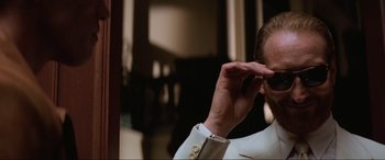 Movie still from “Last Action Hero” (1993), directed by John McTiernan – A man in a white suit is holding his hand up to his face; Close Up shot, Low angle