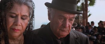 Movie still from “Last Action Hero” (1993), directed by John McTiernan – An older man wearing a hat and a suit; Close Up shot, Over the shoulder angle