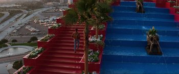 Movie still from “Last Action Hero” (1993), directed by John McTiernan – A man walking down a set of stairs next to a pool; Extreme Wide shot, High angle