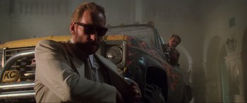 Movie still from “Last Action Hero” (1993), directed by John McTiernan – A man in a suit and sunglasses in front of an old car; Medium shot, Low angle