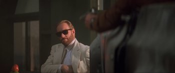 Movie still from “Last Action Hero” (1993), directed by John McTiernan – A man in a white suit and sunglasses is sitting in front of a mirror; Close Up shot, Low angle