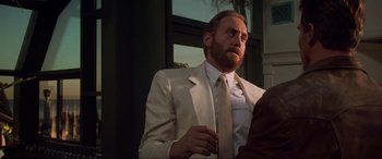 Movie still from “Last Action Hero” (1993), directed by John McTiernan – A man in a suit and tie sitting in front of a window; Medium shot, Over the shoulder angle
