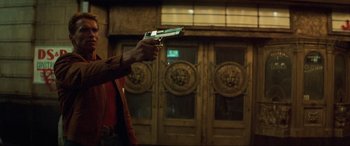 Movie still from “Last Action Hero” (1993), directed by John McTiernan – A man holding a gun in front of a building; Medium shot, Low angle