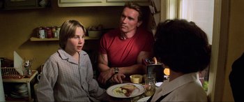 Movie still from “Last Action Hero” (1993), directed by John McTiernan – A group of people sitting at a table with a plate of food on it; Medium shot, Over the shoulder angle