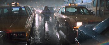 Movie still from “Last Action Hero” (1993), directed by John McTiernan – A man riding a motorcycle down a wet street; Wide shot, Low angle