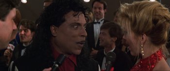 Movie still from “Last Action Hero” (1993), directed by John McTiernan – A man in a red shirt is talking into microphones in front of other men; Close Up shot, Over the shoulder angle