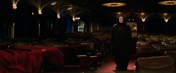 Movie still from “Last Action Hero” (1993), directed by John McTiernan – A man dressed in black standing in front of an empty auditorium; Wide shot, Low angle