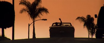 Movie still from “Last Action Hero” (1993), directed by John McTiernan – A person in a car driving down a street at sunset; Extreme Wide shot, Low angle