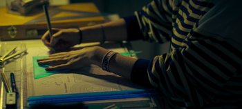 Movie still from “Laura Pausini: Pleasure to Meet You” (2022), directed by Ivan Cotroneo – A person wearing a bracelet sitting at a table; Extreme Close Up shot, High angle