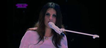 Movie still from “Laura Pausini: Pleasure to Meet You” (2022), directed by Ivan Cotroneo – A woman with long dark brown hair is holding a microphone; Close Up shot, High angle