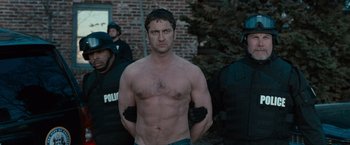 Movie still from “Law Abiding Citizen” (2009), directed by F. Gary Gray – A shirtless man standing in front of a group of police officers; Medium shot, Low angle