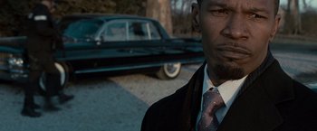 Movie still from “Law Abiding Citizen” (2009), directed by F. Gary Gray – A man wearing a suit and tie standing in front of a car; Close Up shot, Over the shoulder angle