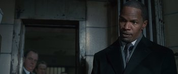 Movie still from “Law Abiding Citizen” (2009), directed by F. Gary Gray – A man wearing a suit and tie standing in front of a building; Close Up shot, Over the shoulder angle