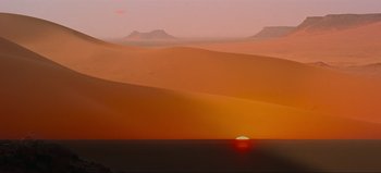 Movie still from “Lawrence of Arabia” (1962), directed by David Lean – The sun is setting in the desert with mountains in the background; Extreme Wide shot, Low angle