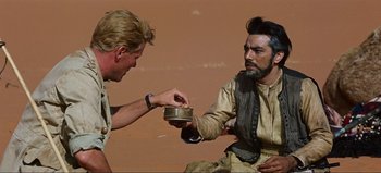 Movie still from “Lawrence of Arabia” (1962), directed by David Lean – A man is holding a bowl and another man is holding a spoon; Medium shot, Over the shoulder angle