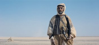 Movie still from “Lawrence of Arabia” (1962), directed by David Lean – A man standing in the middle of the desert holding a rifle; Medium shot, Low angle