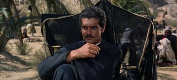 Movie still from “Lawrence of Arabia” (1962), directed by David Lean – A man sitting in a chair with a black umbrella; Medium shot, Over the shoulder angle