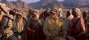 Movie still from “Lawrence of Arabia” (1962), directed by David Lean – A group of men in traditional clothing standing next to each other in the desert; Medium shot, Over the shoulder angle