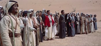 Movie still from “Lawrence of Arabia” (1962), directed by David Lean – A group of men in traditional clothing standing in a desert; Wide shot, Low angle