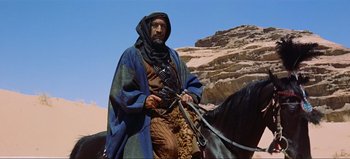 Movie still from “Lawrence of Arabia” (1962), directed by David Lean – A man in a blue and brown robe on a horse; Medium shot, Low angle