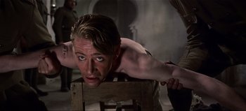Movie still from “Lawrence of Arabia” (1962), directed by David Lean – A shirtless man sitting on a chair with his hands on the back of the chair; Medium shot, Over the shoulder angle