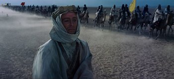 Movie still from “Lawrence of Arabia” (1962), directed by David Lean – A man wearing a turban is standing in front of a herd of horses; Medium shot, Over the shoulder angle