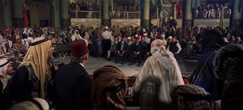 Movie still from “Lawrence of Arabia” (1962), directed by David Lean – A group of people sitting on a stage in front of an audience; Wide shot, High angle