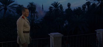 Movie still from “Lawrence of Arabia” (1962), directed by David Lean – A man standing on top of a building near a bunch of palm trees; Wide shot, Over the shoulder angle