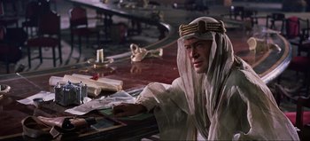 Movie still from “Lawrence of Arabia” (1962), directed by David Lean – A man sitting at a table wearing a head covering; Medium shot, High angle