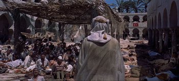 Movie still from “Lawrence of Arabia” (1962), directed by David Lean – A group of people sitting in a field with a man in a robe; Wide shot, High angle