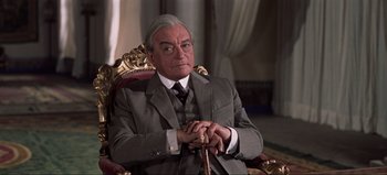 Movie still from “Lawrence of Arabia” (1962), directed by David Lean – An older man sitting in a chair with a cane in his hand; Medium shot, Low angle