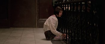 Movie still from “Léon: The Professional” (1994), directed by Luc Besson – A young woman sitting on the ground next to an iron fence; Medium shot, Low angle