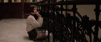 Movie still from “Léon: The Professional” (1994), directed by Luc Besson – A woman sitting on the ground smoking a cigarette in front of an iron railing; Wide shot, Low angle