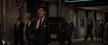 Movie still from “Léon: The Professional” (1994), directed by Luc Besson – A man wearing a suit and hat standing next to a mailbox; Medium shot, Low angle