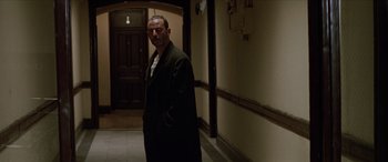 Movie still from “Léon: The Professional” (1994), directed by Luc Besson – A man standing in a hallway with a coat on; Medium shot, Low angle