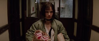 Movie still from “Léon: The Professional” (1994), directed by Luc Besson – A woman in a green jacket holding a bag of food; Medium shot, Low angle
