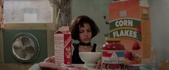 Movie still from “Léon: The Professional” (1994), directed by Luc Besson – A woman sitting at a table with a bowl of cereal; Medium shot, Low angle