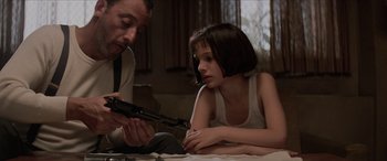 Movie still from “Léon: The Professional” (1994), directed by Luc Besson – A man and a girl are looking at a gun; Medium shot, Low angle