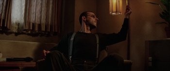 Movie still from “Léon: The Professional” (1994), directed by Luc Besson – A man sitting on a couch in a living room; Medium shot, Low angle