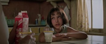 Movie still from “Léon: The Professional” (1994), directed by Luc Besson – A young woman sitting at a table with a glass of milk in front of her; Close Up shot, Over the shoulder angle