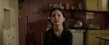 Movie still from “Léon: The Professional” (1994), directed by Luc Besson – A young person sitting in a room with a shelf in the background; Close Up shot, Over the shoulder angle