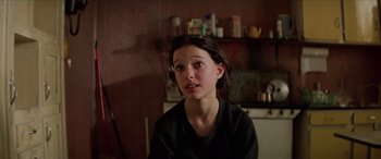 Movie still from “Léon: The Professional” (1994), directed by Luc Besson – A young woman sitting in front of a shelf; Close Up shot, Over the shoulder angle