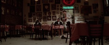Movie still from “Léon: The Professional” (1994), directed by Luc Besson – A man standing in front of a table in a restaurant; Wide shot, High angle
