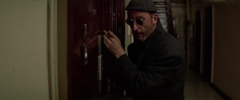 Movie still from “Léon: The Professional” (1994), directed by Luc Besson – A man in a hat and sunglasses looking into a door; Close Up shot, Low angle