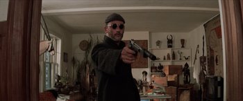 Movie still from “Léon: The Professional” (1994), directed by Luc Besson – A man holding a gun while wearing a hat and sunglasses; Medium shot, Low angle