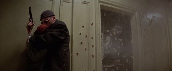 Movie still from “Léon: The Professional” (1994), directed by Luc Besson – A man standing in front of a wall covered in bullet holes; Medium shot, Low angle