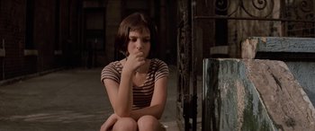 Movie still from “Léon: The Professional” (1994), directed by Luc Besson – A girl sitting on the ground with her hand on her chin; Close Up shot, High angle