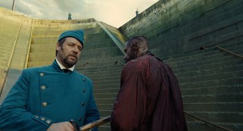 Movie still from “Les Misérables” (2012), directed by Tom Hooper – Two men standing next to each other near a stone wall; Medium shot, Over the shoulder angle