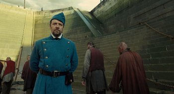 Movie still from “Les Misérables” (2012), directed by Tom Hooper – A man in a blue uniform standing in front of two other men; Medium shot, Low angle